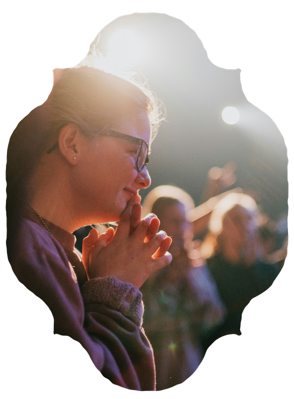 A woman in warm light, hands clasped, among an audience