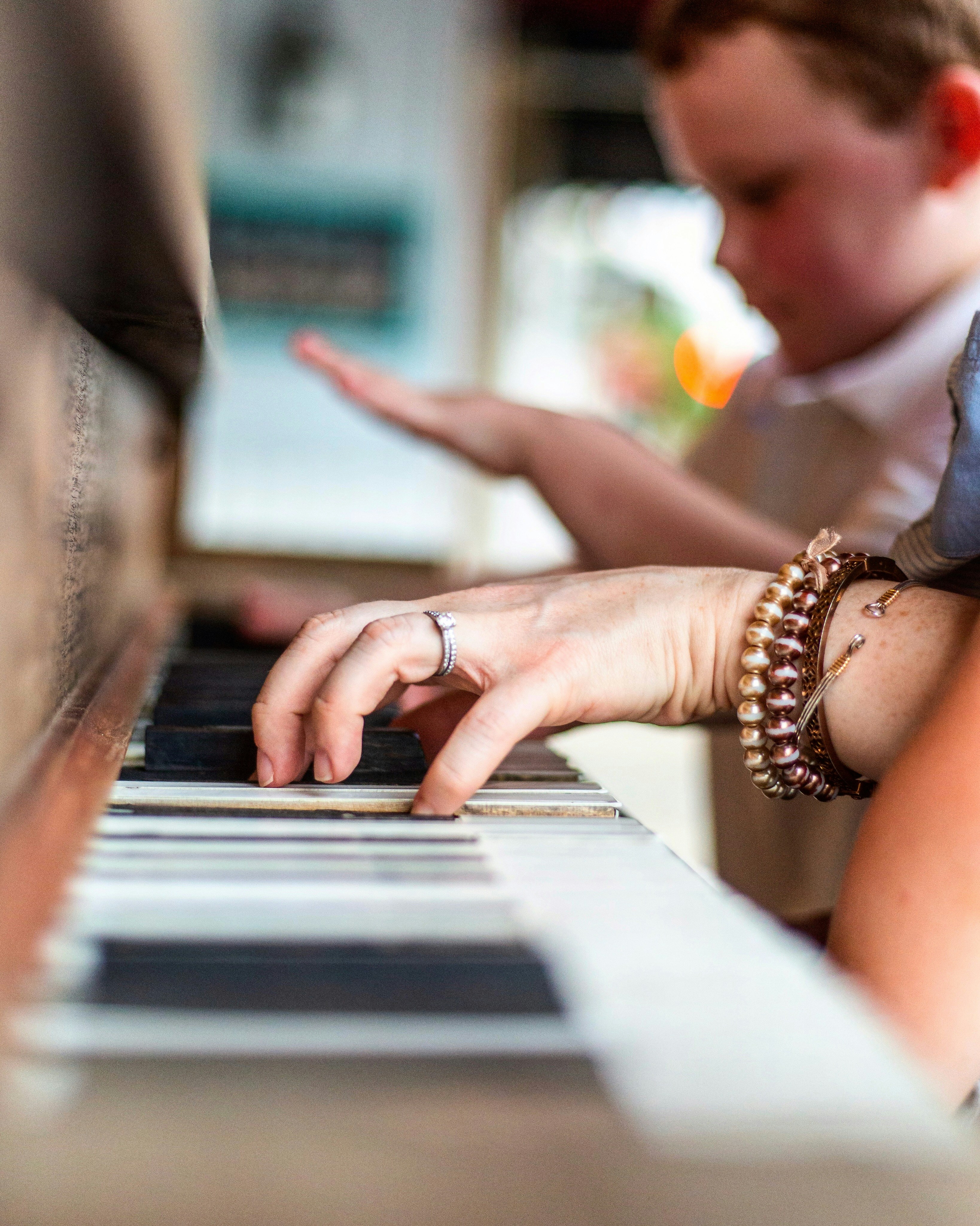 Hands at a piano keyboard while a child watches
