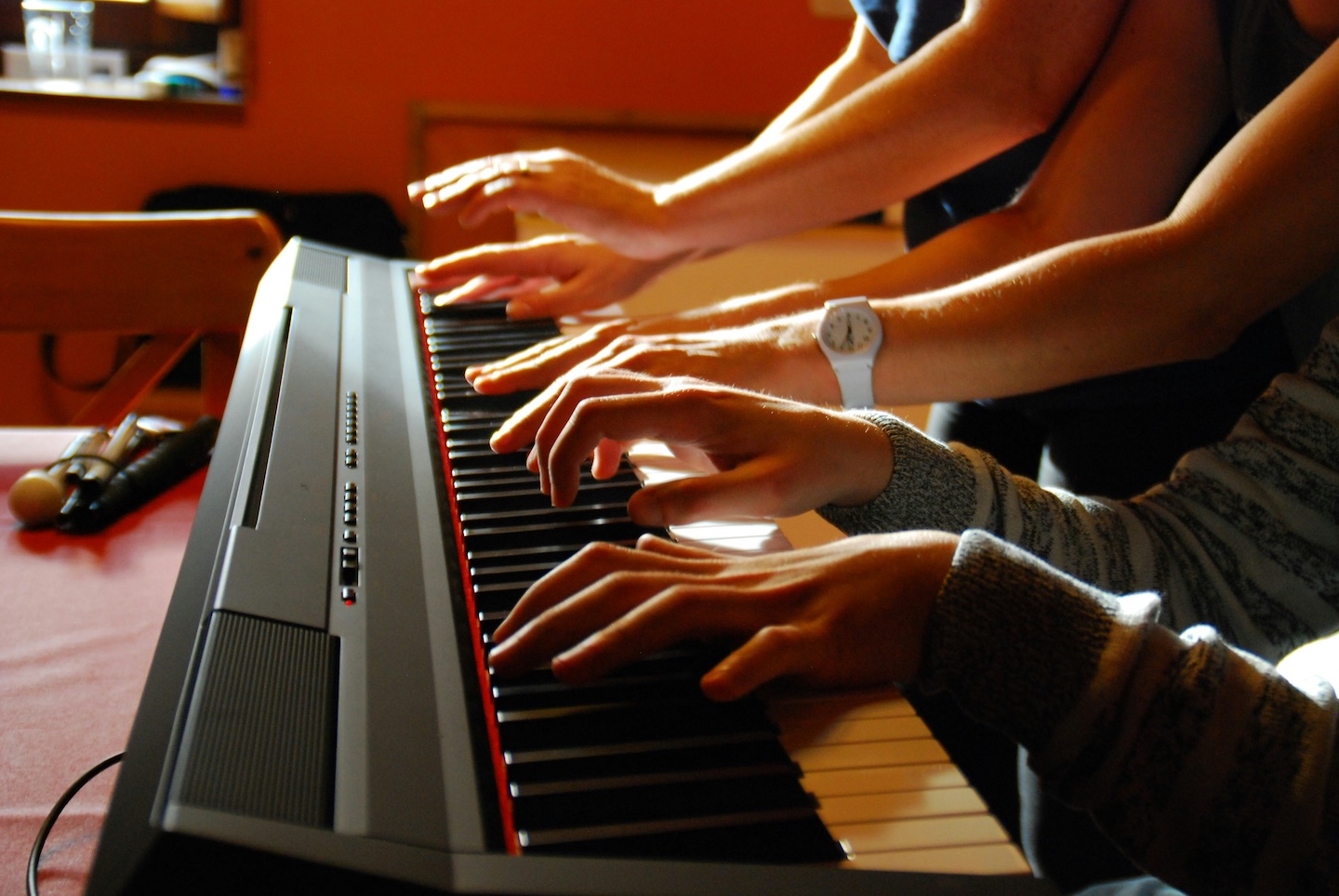 Several pairs of hands sharing one keyboard at a digital piano